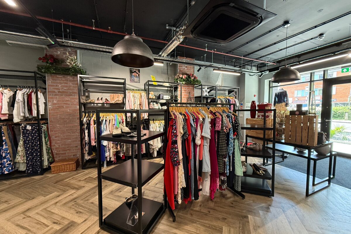 Modern charity shop interior with freestanding display black metal clothing rails and shelving, displaying colourful garments in a bright, open retail space.
