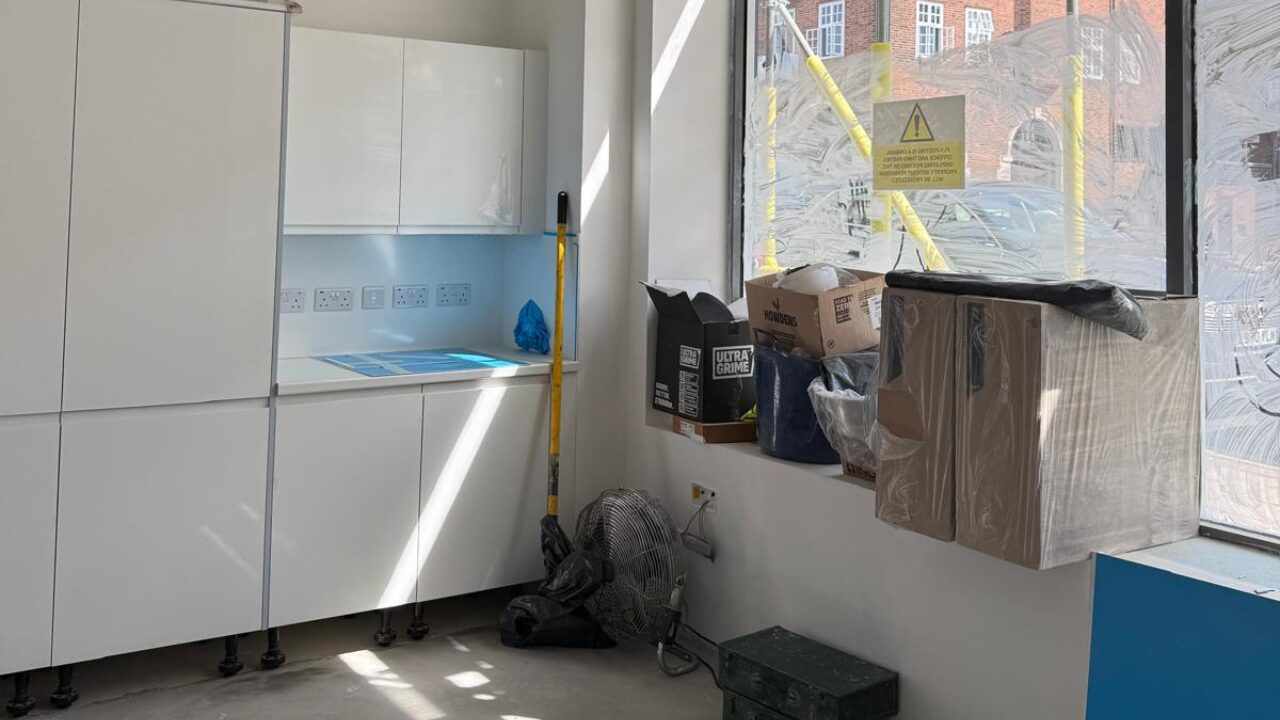 Commercial fit-out in progress showing a newly installed office kitchenette with cabinetry, unfinished flooring, and construction materials during the build phase.
