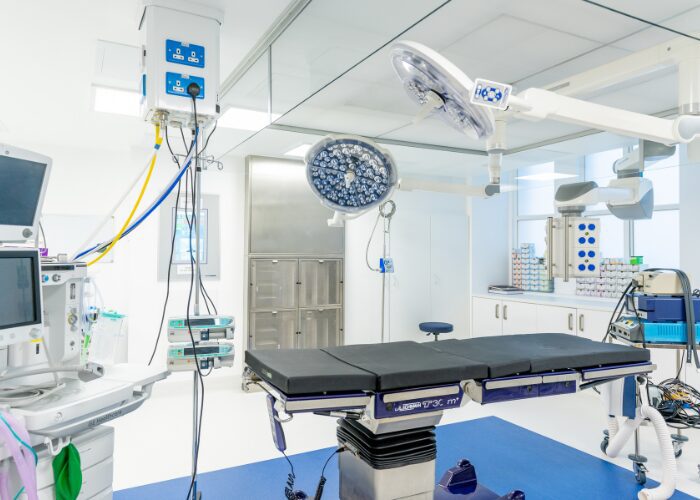 Modern private hospital operating theatre with surgical lights, operating table, medical equipment and clinical storage.